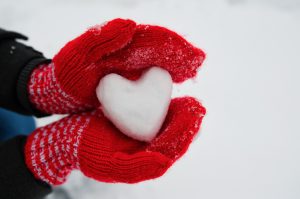 red female gloves hold a white heart from the snow.