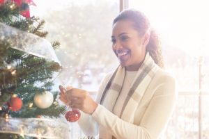 Beautiful woman hangs ornament on Christmas tree at home